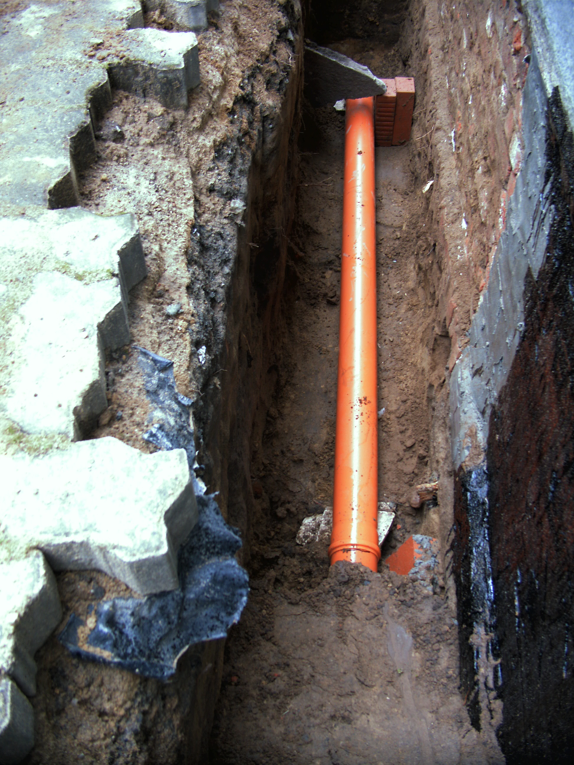 Regenwasser-Verrohrung außen mit Kellerwandabdichtung durch Verputzen und Teeren.